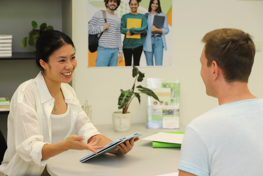 Studienberaterin berät Studenten an einem Tisch. Die Studienberaterin hält ein Tablet in der Hand.
